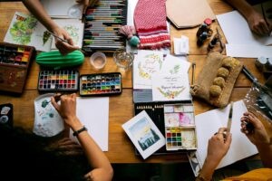 Top view of artists working with watercolor paints and art supplies in a creative workshop setting.